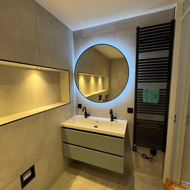 Badkamer met ronde spiegel, wastafelmeubel, verlichte nis en zwarte designradiator