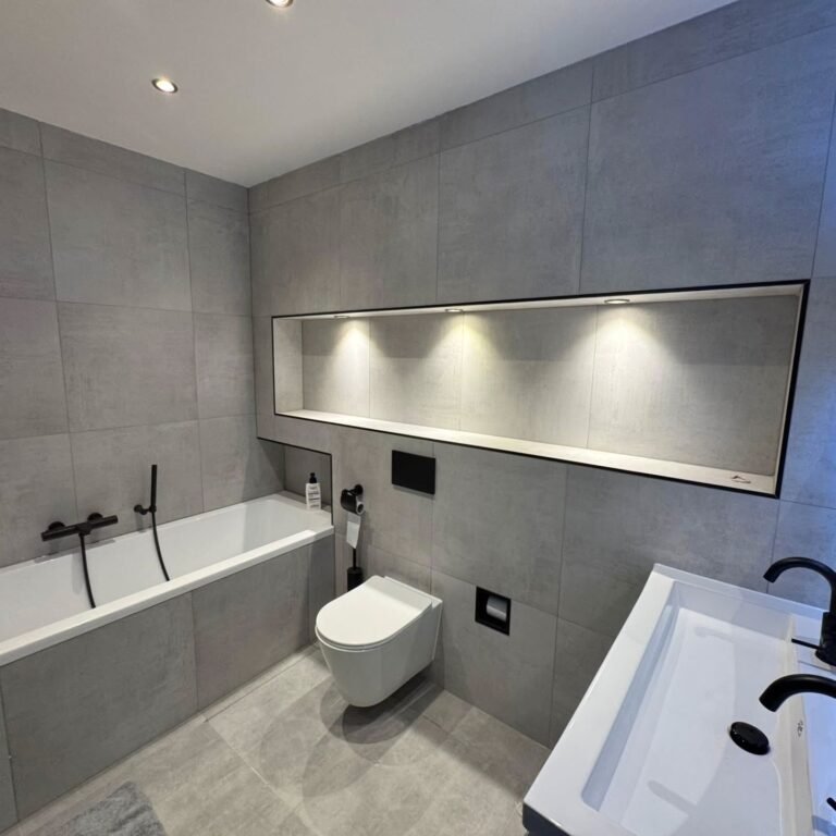 Badkamer met ligbad, hangend toilet, grijze tegels en verlichte wandnis