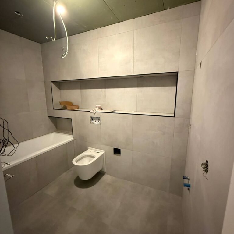Badkamer met bad, hangend toilet en verlichte nis in grijze tegels