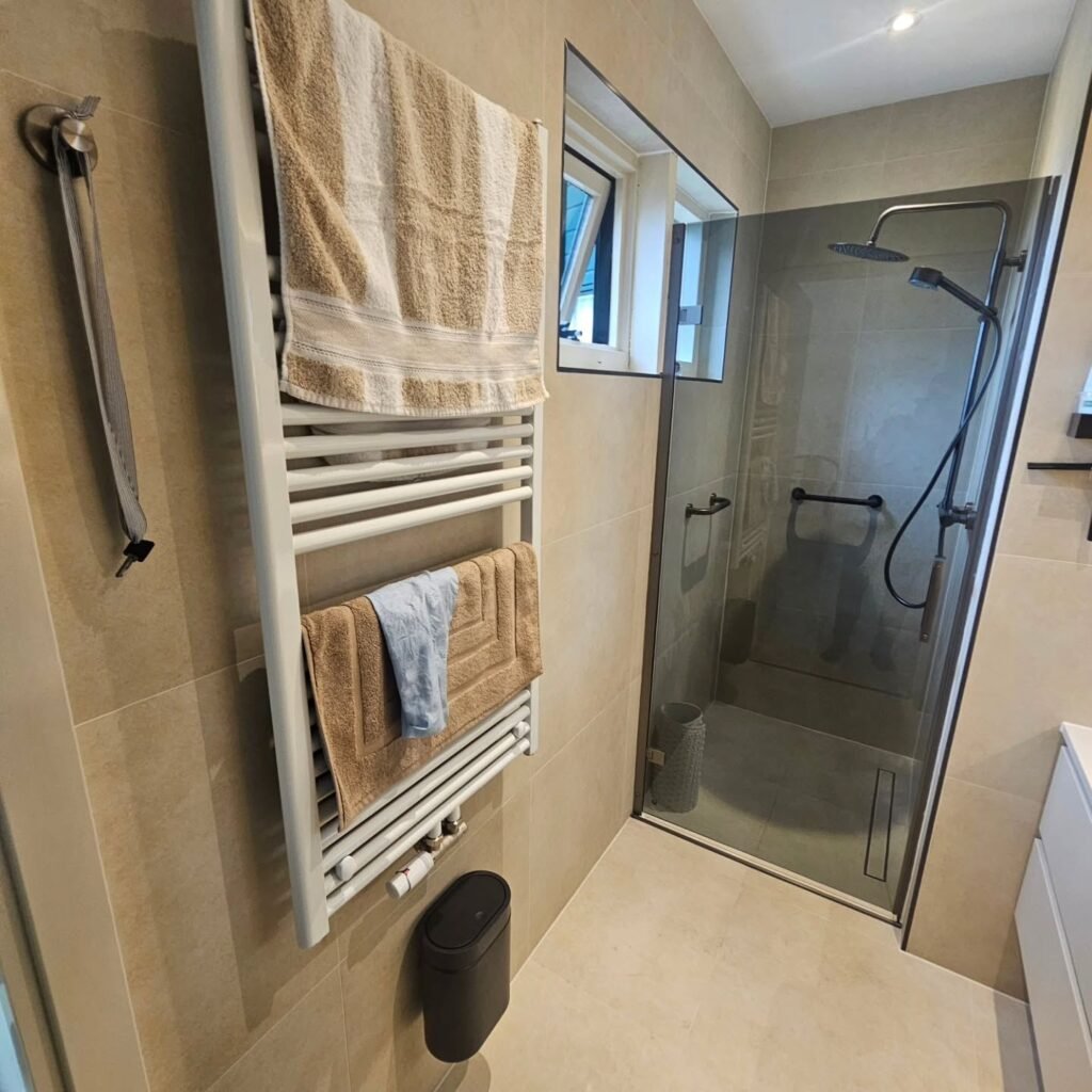 Douche met glazen wand en handdoekradiator in een badkamer