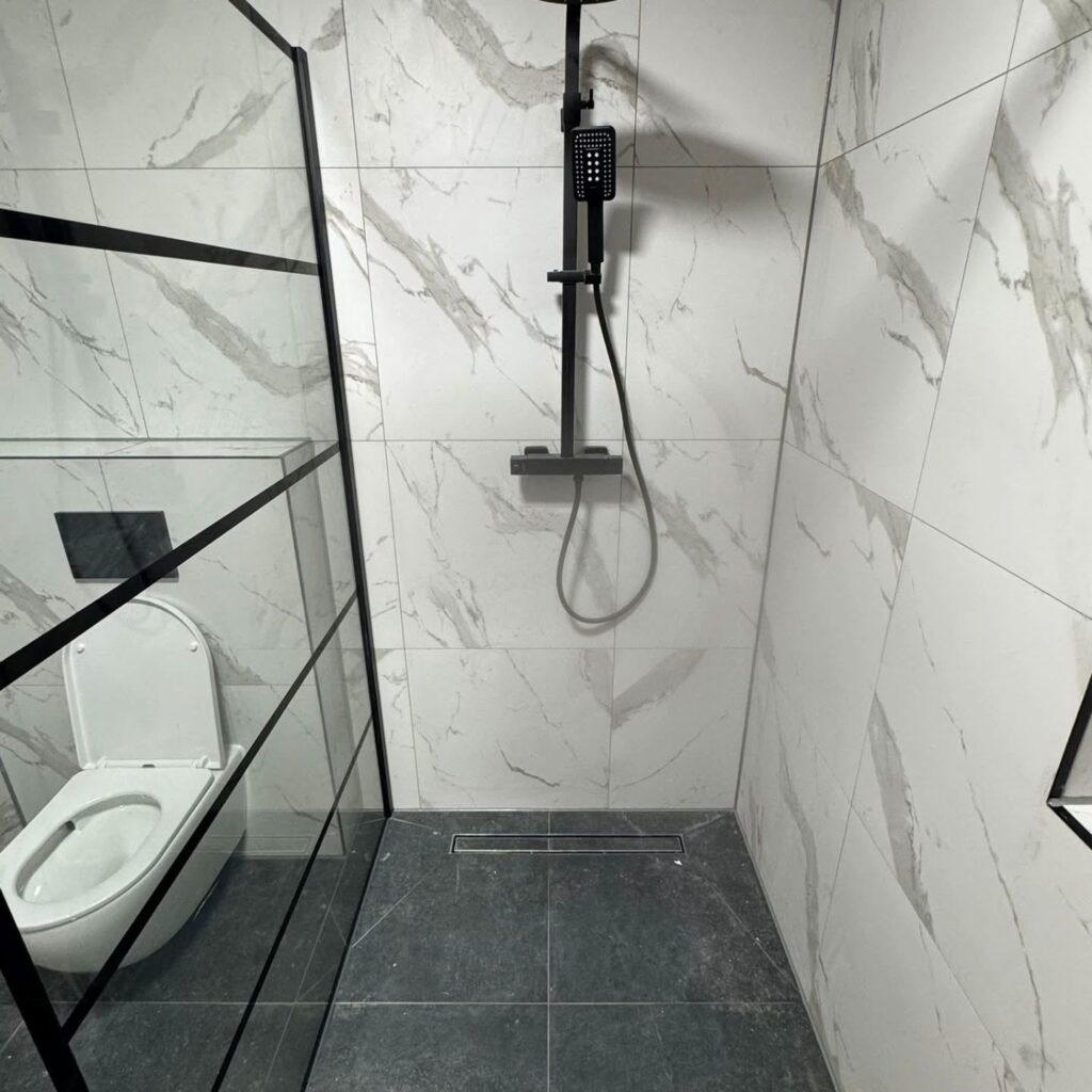 Inloopdouche met marmerlook tegels en zwart stalen raam naast een hangend toilet
