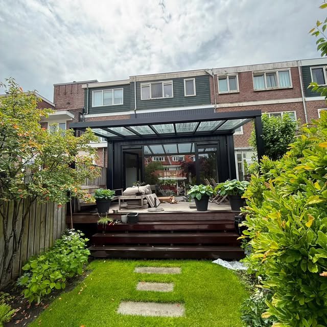 Achtertuin met overkapping met glazen dak en houten terras